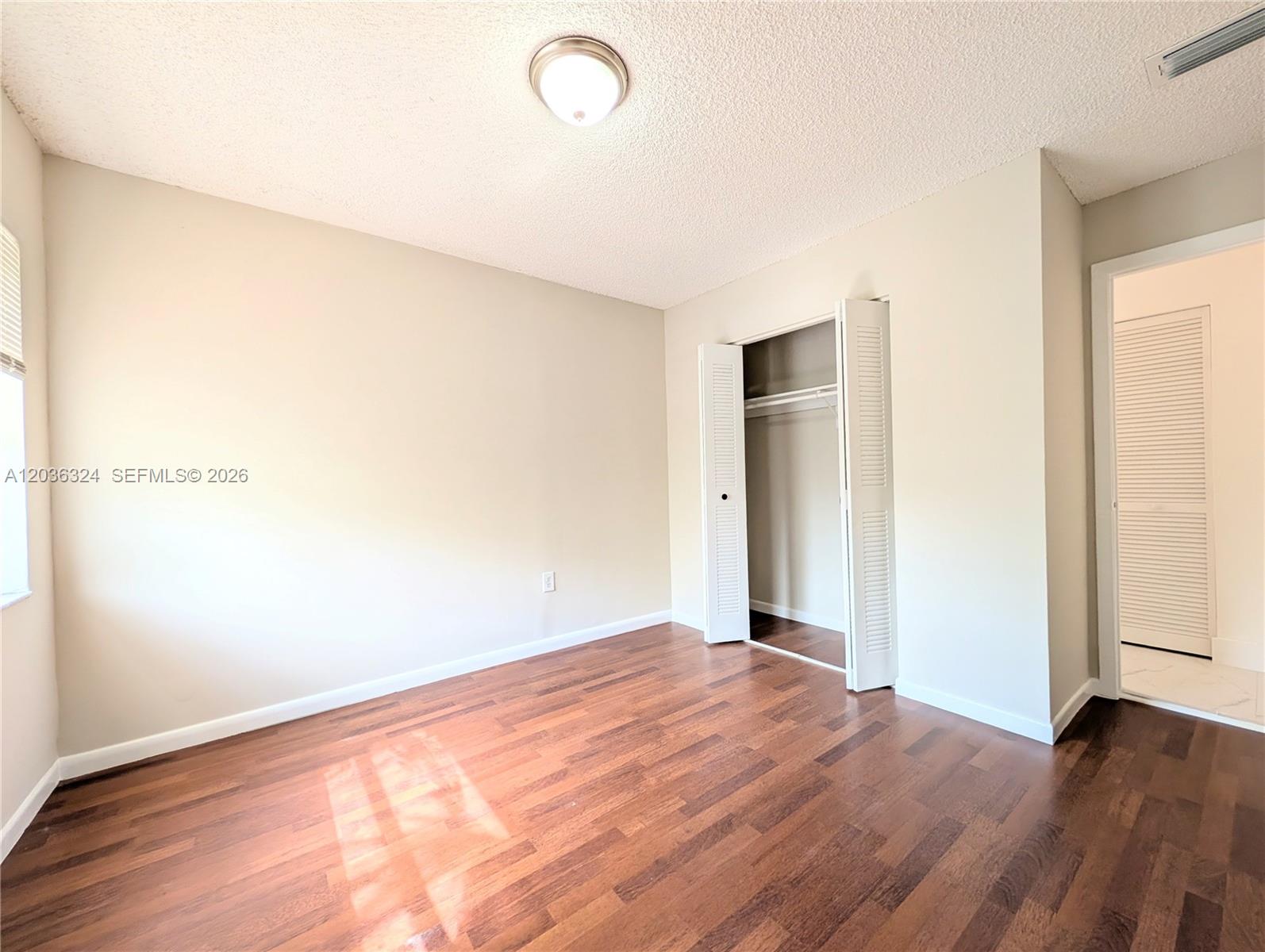 An empty bedroom features wood-look flooring, a ceiling light, and a closet with louvered doors — 58 SW 14th Ter, Homestead FL 33030, HOMESTEAD, FL