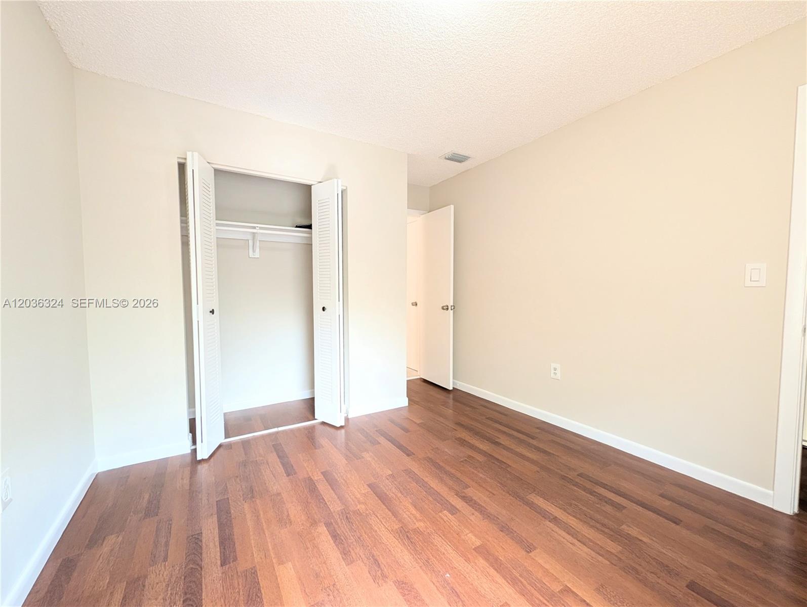 An empty bedroom features wood-look flooring, beige walls, a closet, and a doorway — 58 SW 14th Ter, Homestead FL 33030, HOMESTEAD, FL