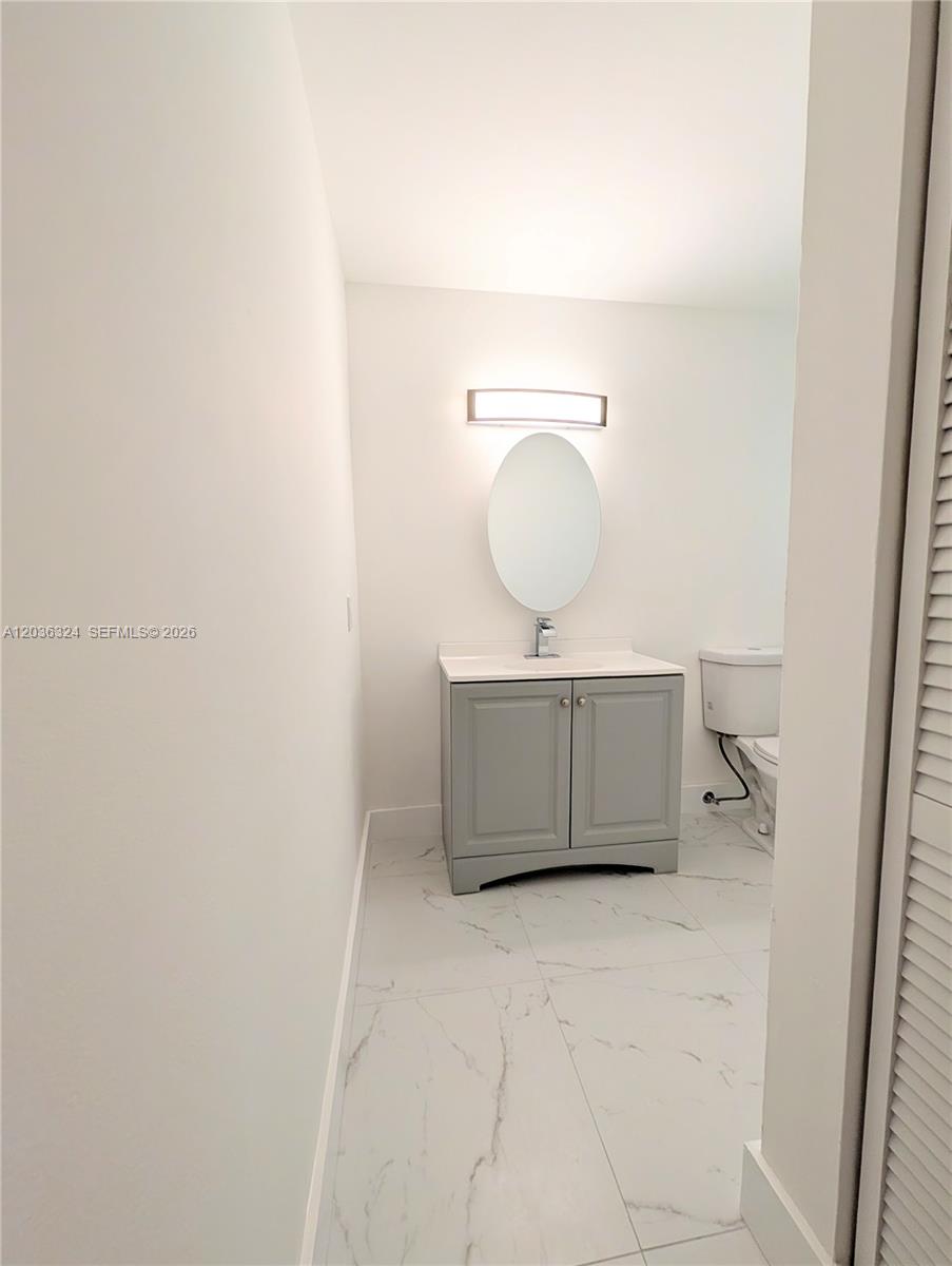 A bathroom features a gray vanity, an oval mirror, and white marble-patterned floor tiles — 58 SW 14th Ter, Homestead FL 33030, HOMESTEAD, FL
