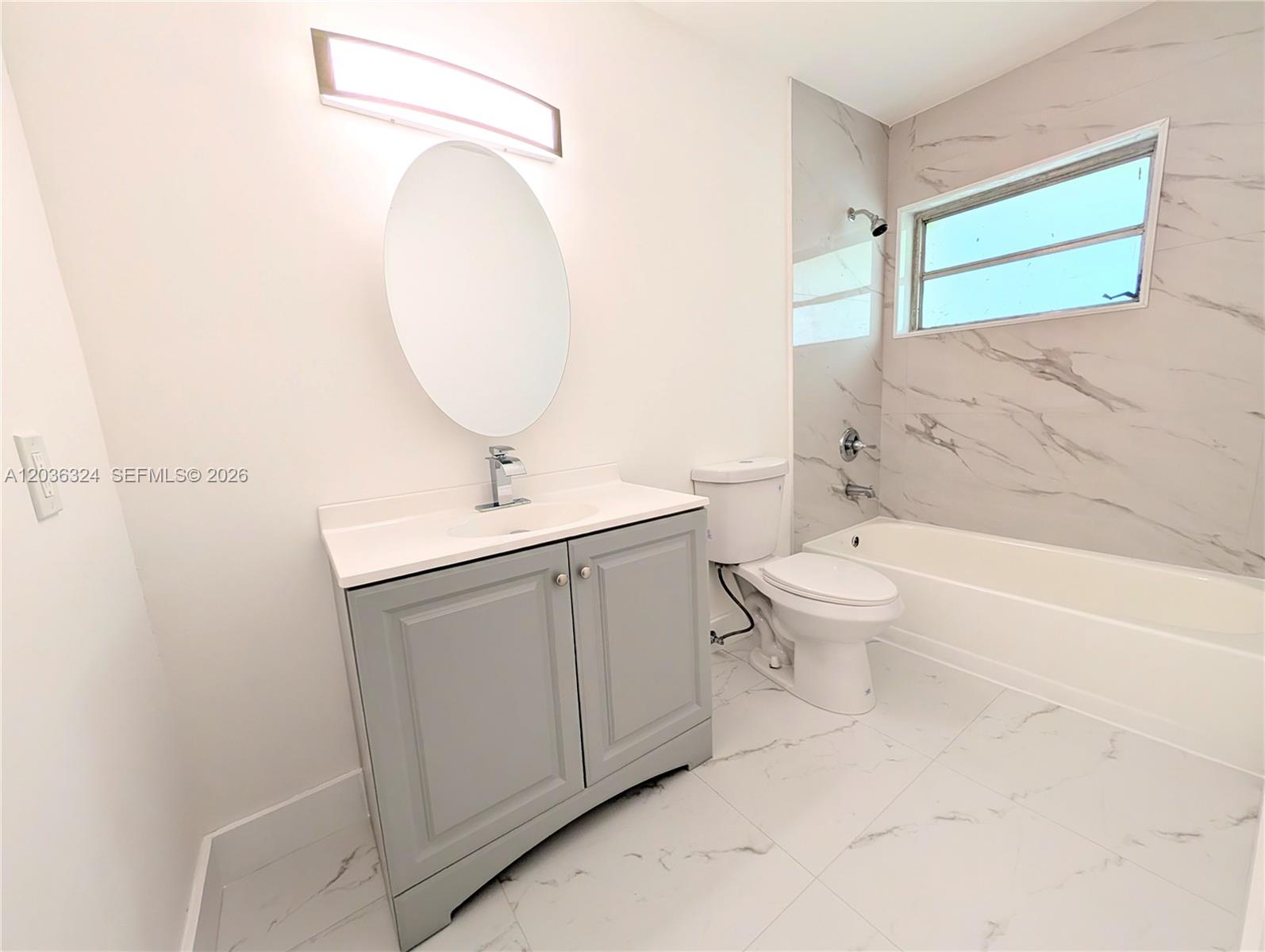 A bathroom features a gray vanity, oval mirror, white toilet, and a marble-tiled bathtub area — 58 SW 14th Ter, Homestead FL 33030, HOMESTEAD, FL