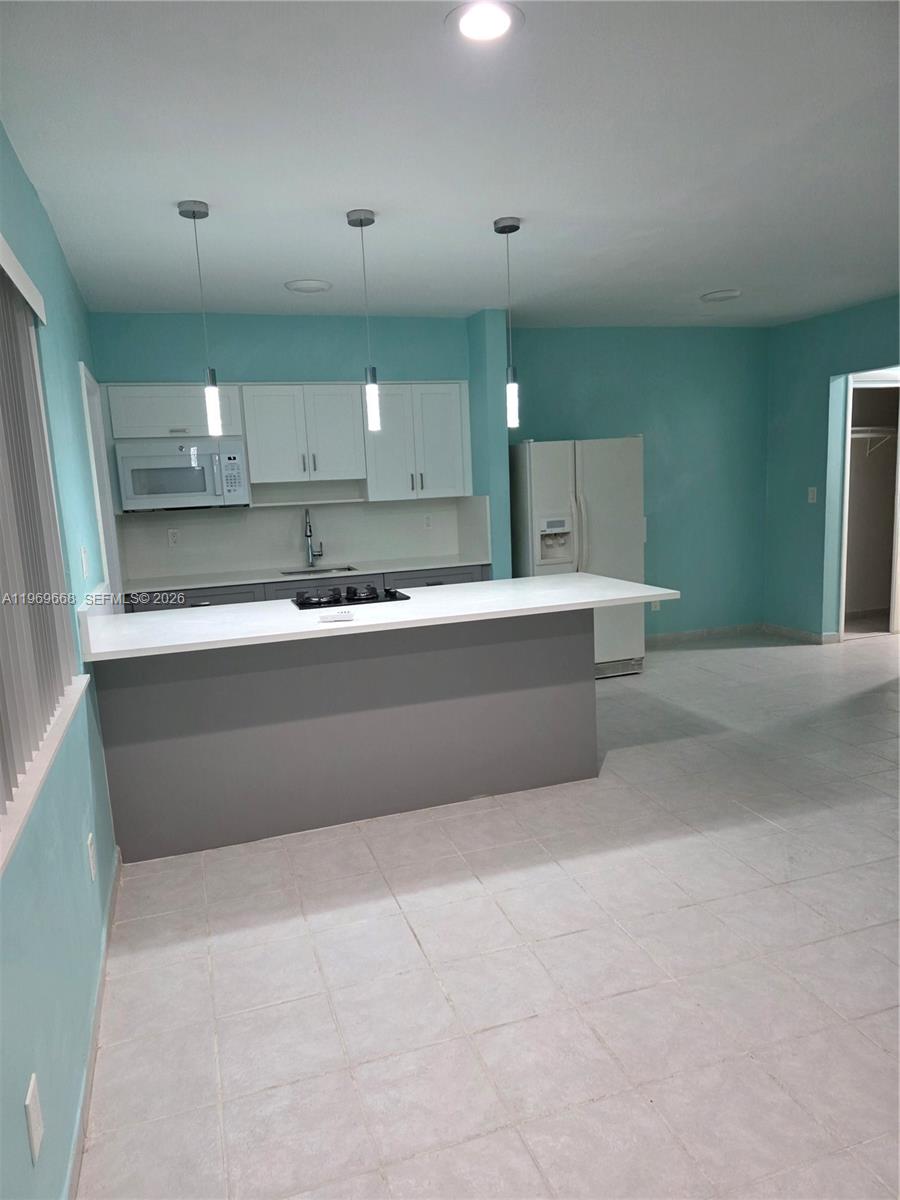 A kitchen features a gray island, white cabinets, light blue walls, and tile flooring — 2101 Calais Dr # 8, Miami Beach FL 33141, MIAMI BEACH, FL