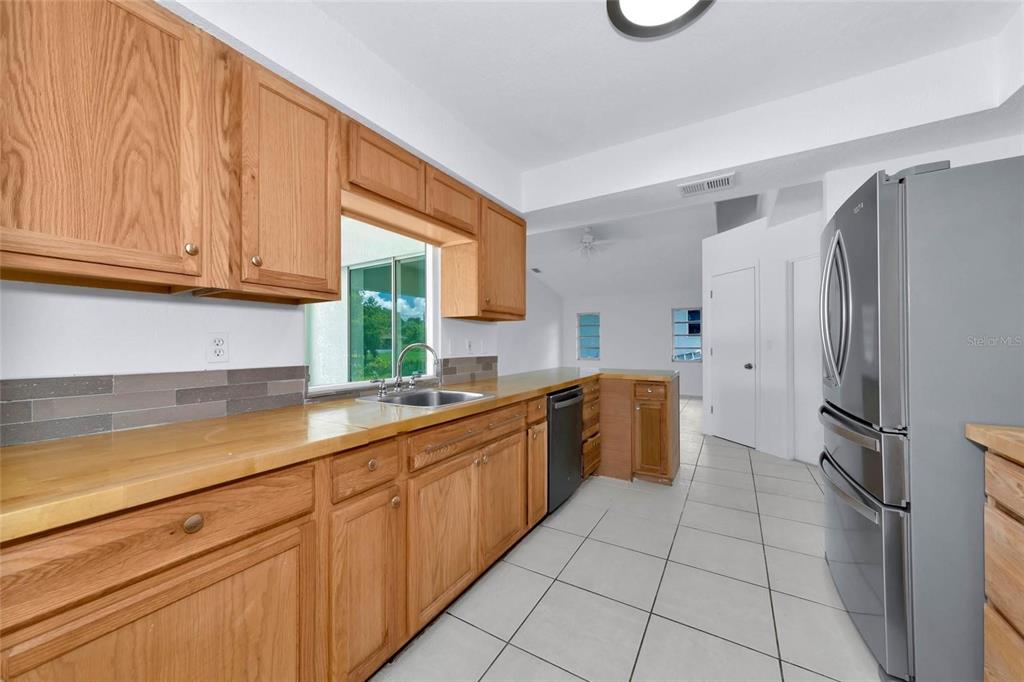 A kitchen features wood cabinets, a light-colored countertop, a stainless steel refrigerator, and tile flooring — 4819 WECOMA AVENUE, NORTH PORT, FL