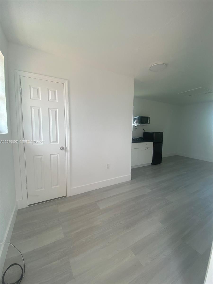 A room with light wood-look flooring, a white door, and a small kitchenette area — 15130 Tyler St, Miami FL 33176, MIAMI, FL