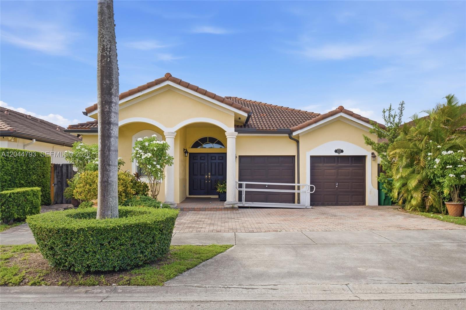 A yellow single-story house features a tile roof, two garage doors, and a wheelchair ramp — 15125 SW 12th Ter, Miami FL 33194, MIAMI, FL