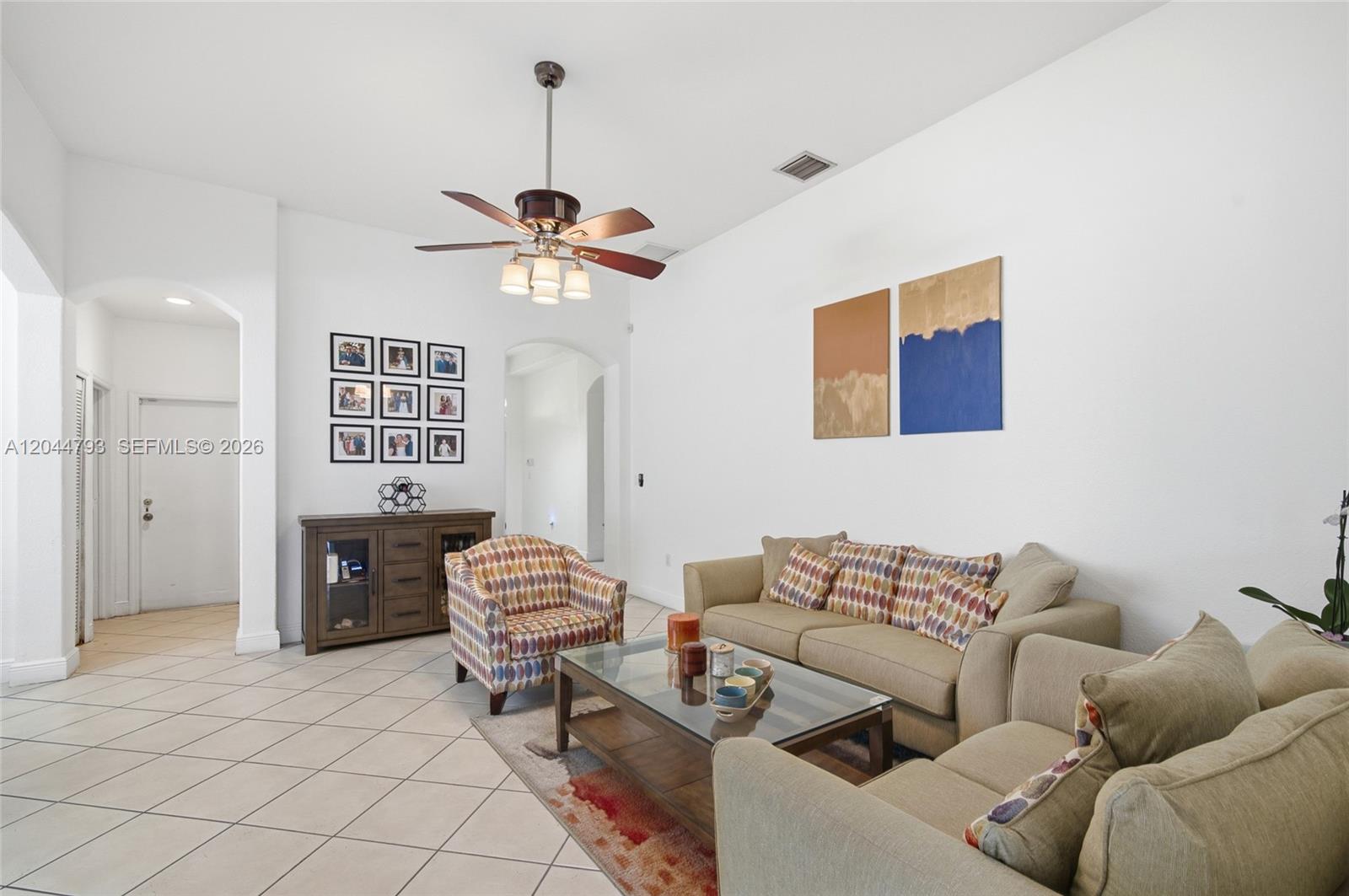 A living room features a beige sofa, patterned armchair, glass coffee table, and tile flooring — 15125 SW 12th Ter, Miami FL 33194, MIAMI, FL