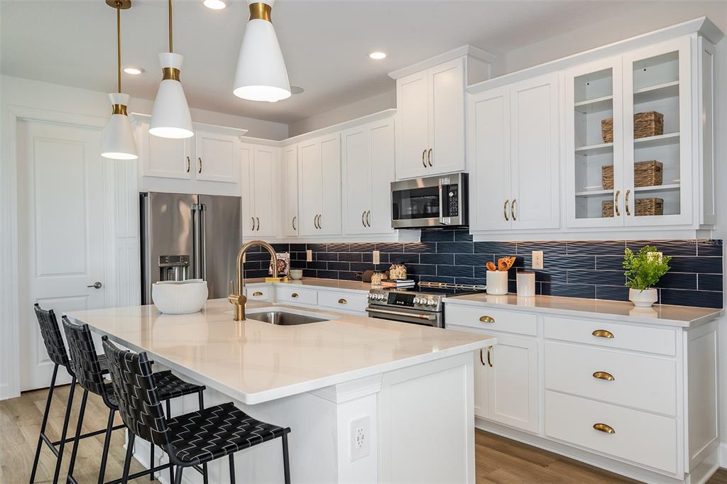 A modern kitchen features white cabinetry, a quartz island, and a dark blue tiled backsplash — 26116 ASPARANO AVENUE, ENGLEWOOD, FL
