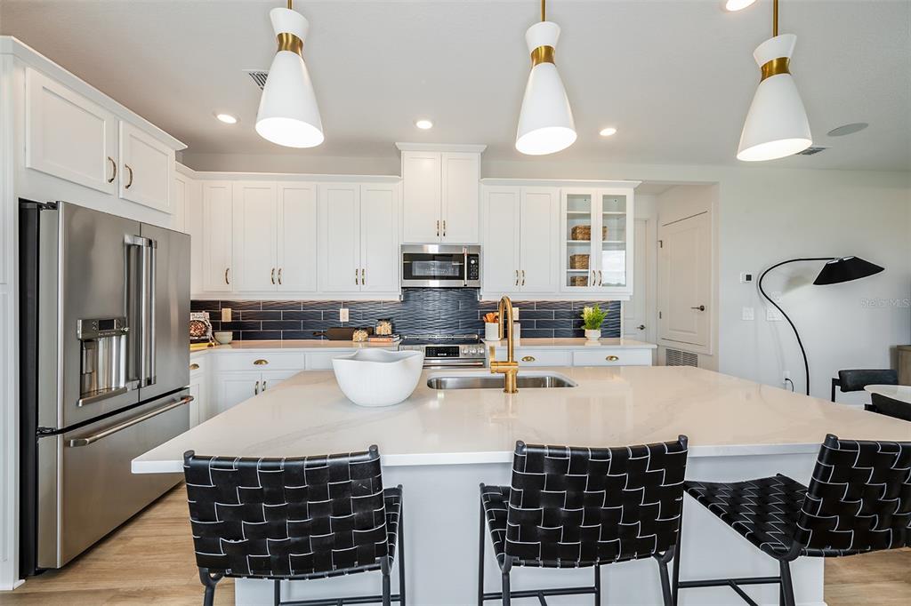 A modern kitchen features white cabinetry, a large quartz island, and dark blue tile backsplash — 26116 ASPARANO AVENUE, ENGLEWOOD, FL