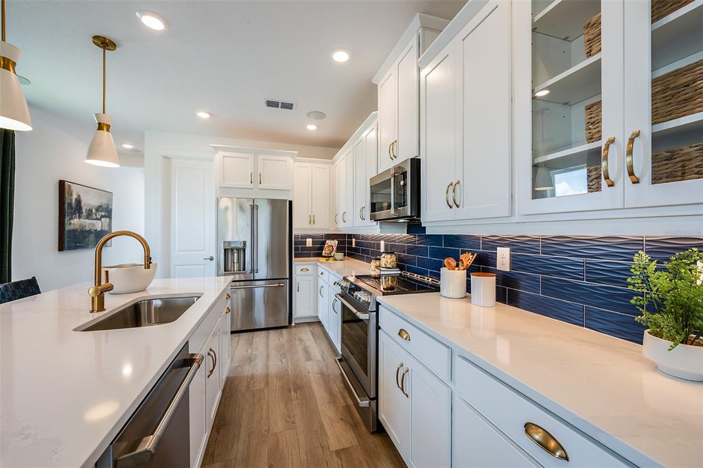A modern kitchen features white cabinetry, stainless steel appliances, a quartz island, and blue tile — 26116 ASPARANO AVENUE, ENGLEWOOD, FL