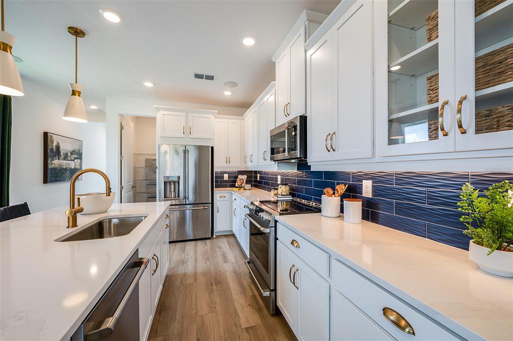 A modern kitchen features white cabinetry, quartz countertops, a blue tiled backsplash, and stainless appliances — 26116 ASPARANO AVENUE, ENGLEWOOD, FL