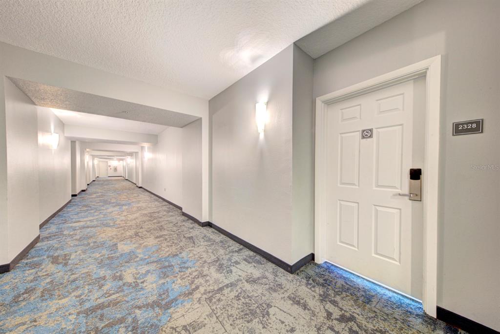 A long hotel hallway features patterned blue and gray carpeting and a white door numbered 2328 — 350 N ATLANTIC AVENUE UNIT 2328, DAYTONA BEACH, FL