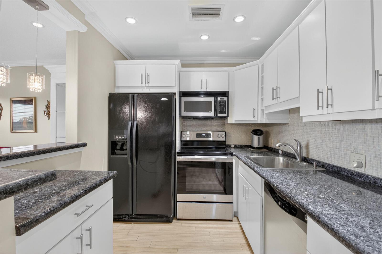 A kitchen features white cabinets, dark granite countertops, stainless steel appliances, and a black refrigerator — 125 Suffolk C, Boca Raton FL 33434, BOCA RATON, FL