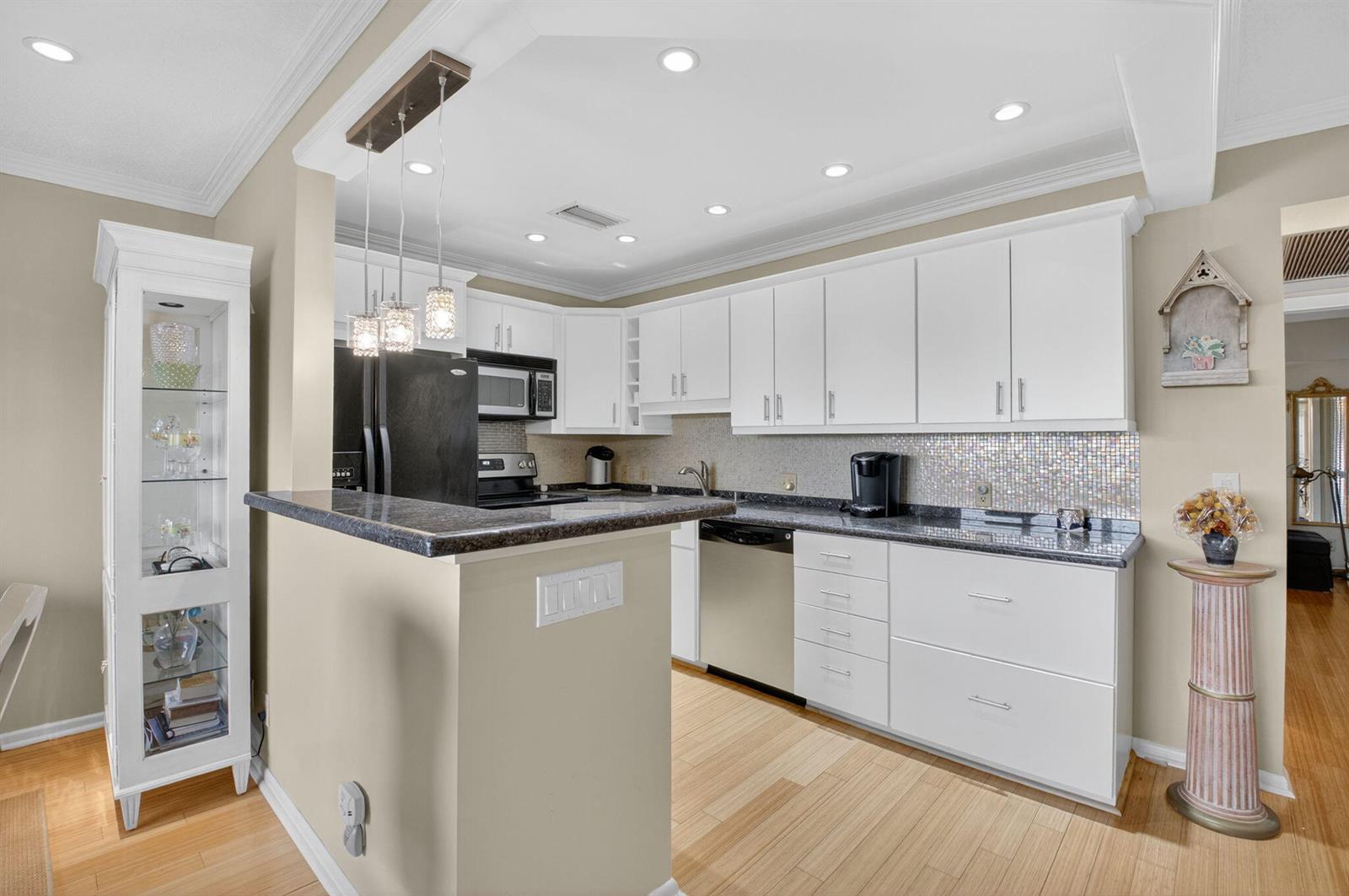A kitchen features white cabinets, dark granite countertops, stainless steel appliances, and light wood flooring — 125 Suffolk C, Boca Raton FL 33434, BOCA RATON, FL