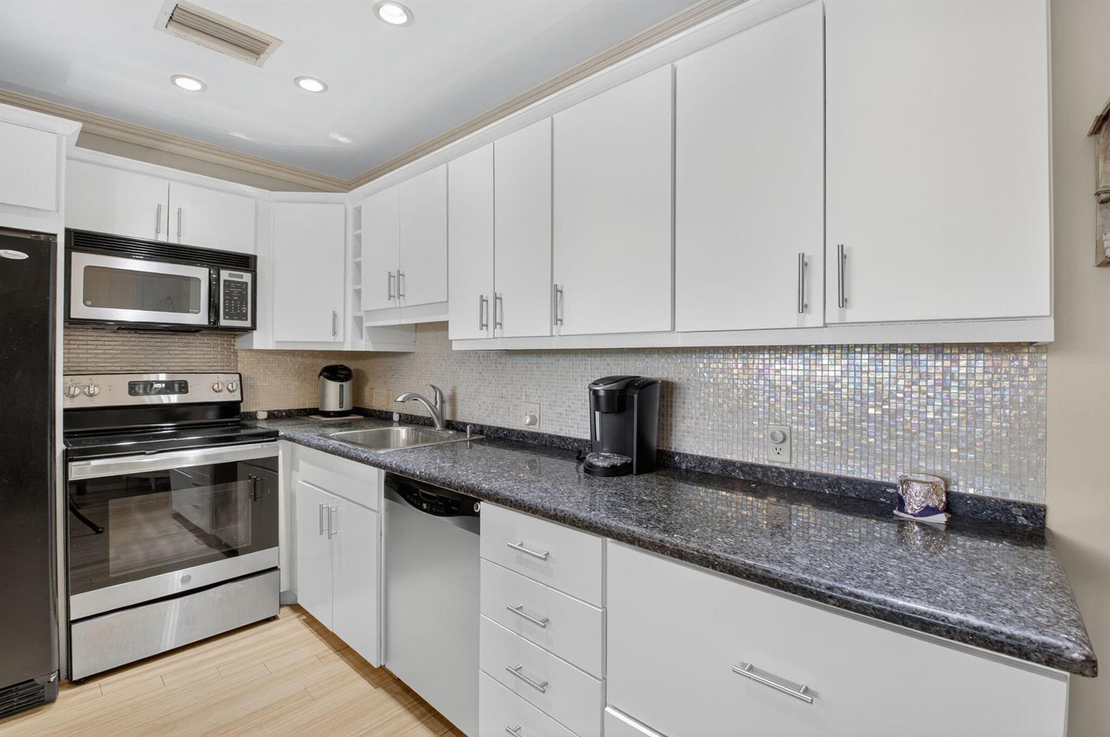 A kitchen with white cabinets, dark granite countertops, stainless steel appliances, and a tiled backsplash — 125 Suffolk C, Boca Raton FL 33434, BOCA RATON, FL