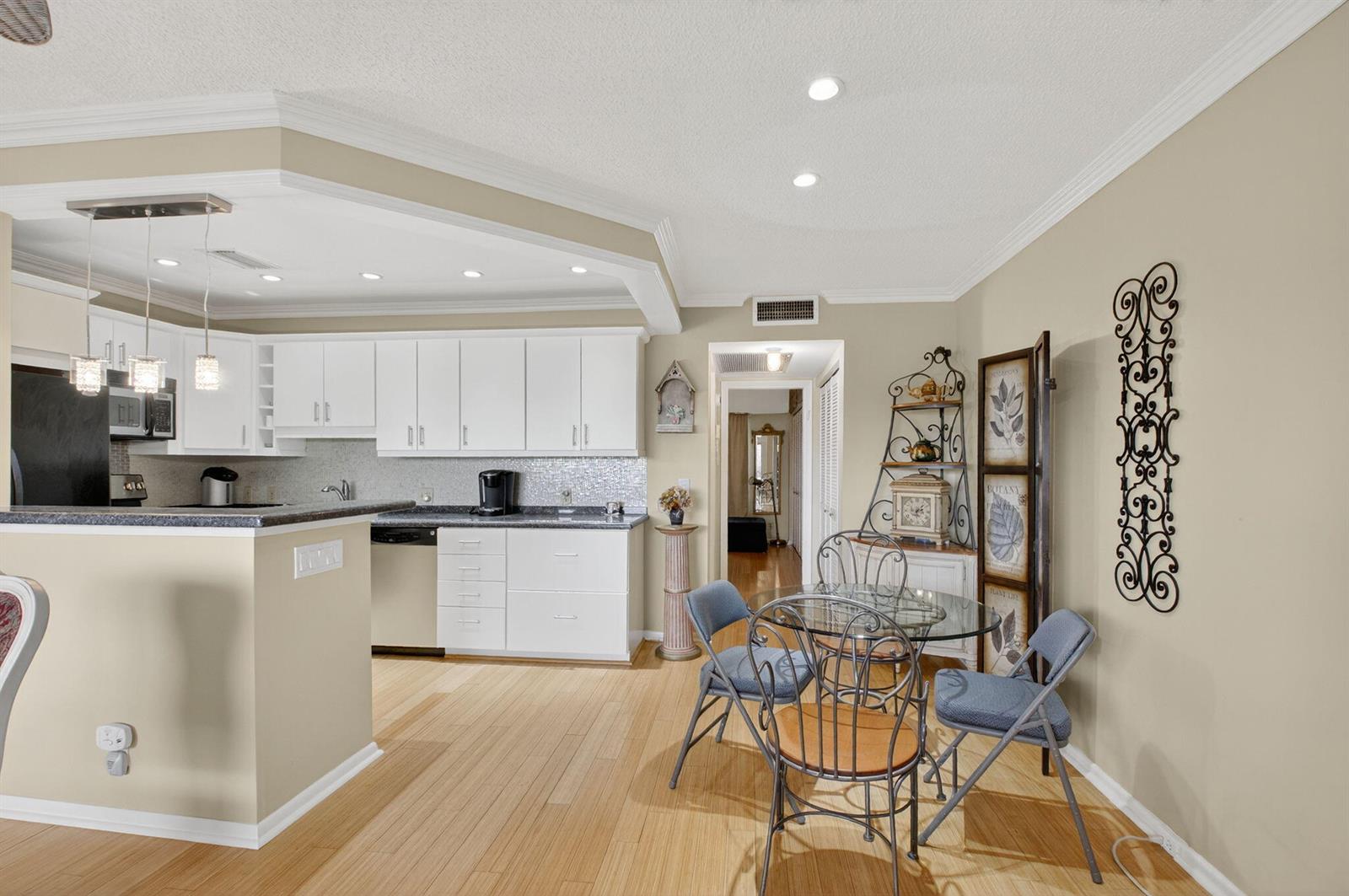 A kitchen with white cabinets and a dining area with a glass table and chairs — 125 Suffolk C, Boca Raton FL 33434, BOCA RATON, FL