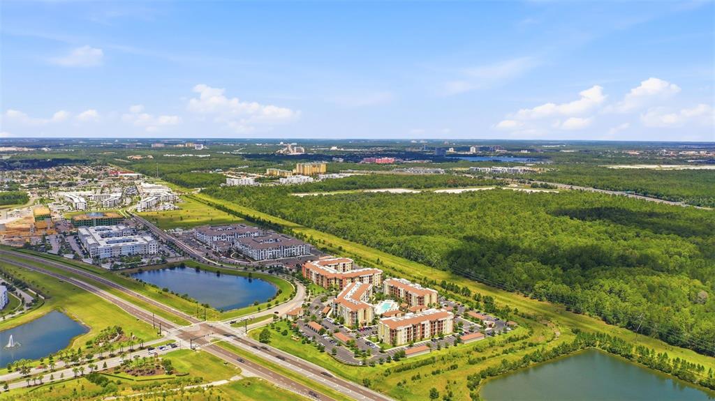 An aerial view shows apartment complexes, ponds, and surrounding forest under a blue sky — S APOPKA VINELAND ROAD, ORLANDO, FL