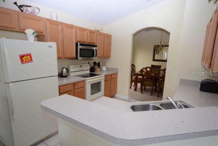 A kitchen features light wood cabinets, white appliances, and a peninsula counter overlooking a dining area — 137 ROSSO DRIVE, DAVENPORT, FL
