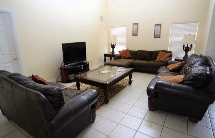 A living room with tile flooring, dark leather furniture, a coffee table, and high ceilings — 137 ROSSO DRIVE, DAVENPORT, FL