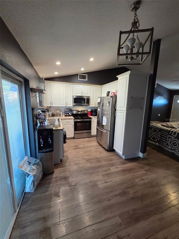 A kitchen features white cabinets, stainless steel appliances, and wood-look flooring under a vaulted ceiling — 3101 SEVEN SPRINGS BOULEVARD, NEW PORT RICHEY, FL