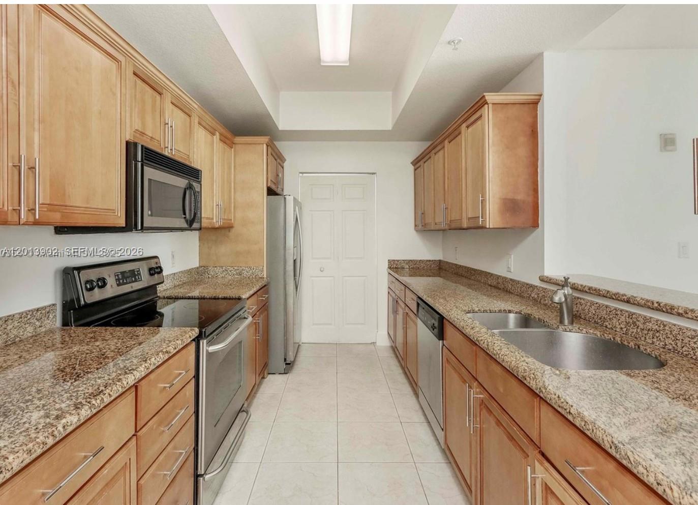A galley kitchen features light wood cabinets, granite countertops, and stainless steel appliances — 3590 Coral Way # 910, Miami FL 33145, MIAMI, FL