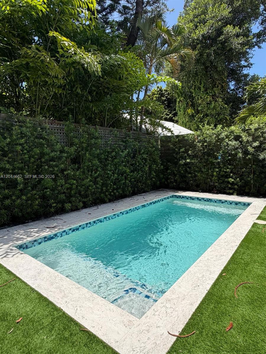 A rectangular swimming pool with a light-colored stone deck is surrounded by lush green landscaping — 2401 SW 16th Ct, Miami FL 33145, MIAMI, FL