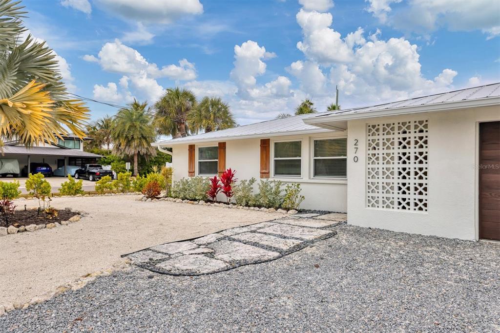 A white house with a metal roof, decorative breeze block wall, and gravel driveway — 270 GLADIOLUS STREET, ANNA MARIA, FL