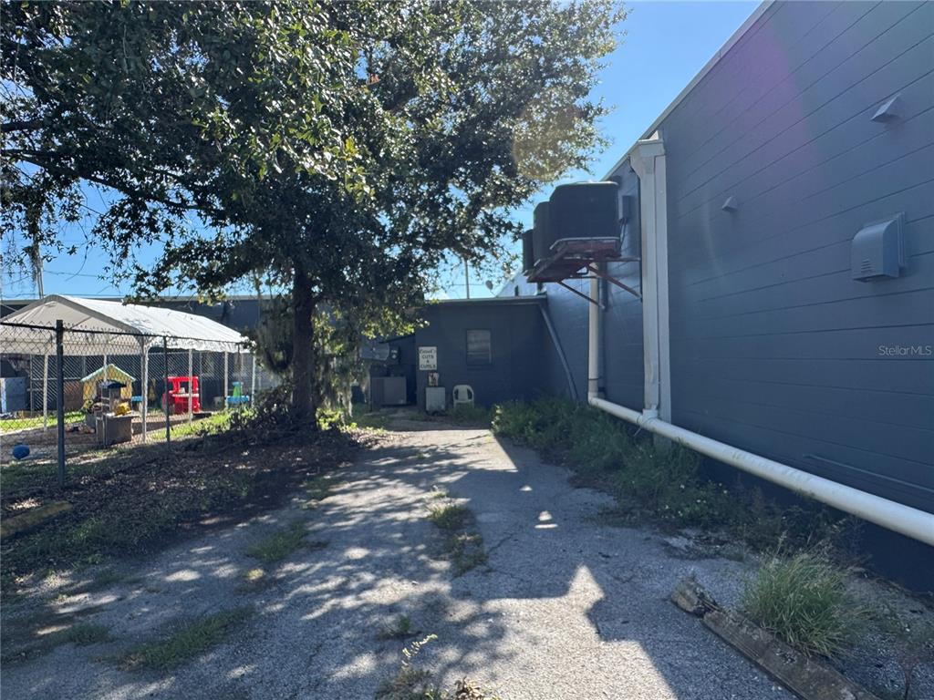 A paved path leads alongside a dark-sided building with exterior HVAC units and a fenced playground — 205 N SCENIC HIGHWAY, FROSTPROOF, FL