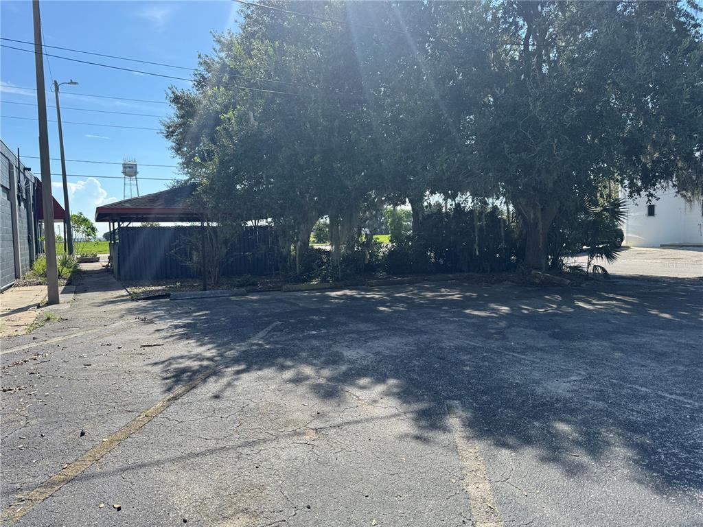 An asphalt parking lot sits in front of a shaded outdoor structure and large trees — 205 N SCENIC HIGHWAY, FROSTPROOF, FL