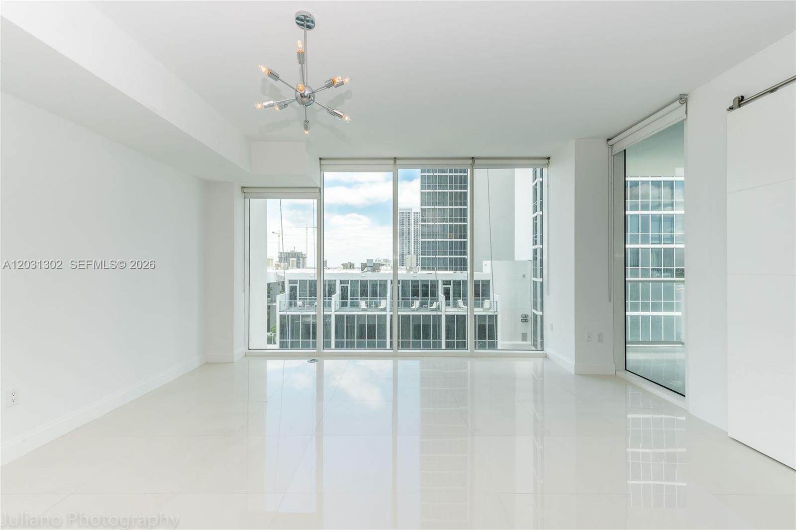 An empty room features white tile floors, a modern chandelier, and floor-to-ceiling windows — 1040 Biscayne Blvd # 1205, Miami FL 33132, MIAMI, FL
