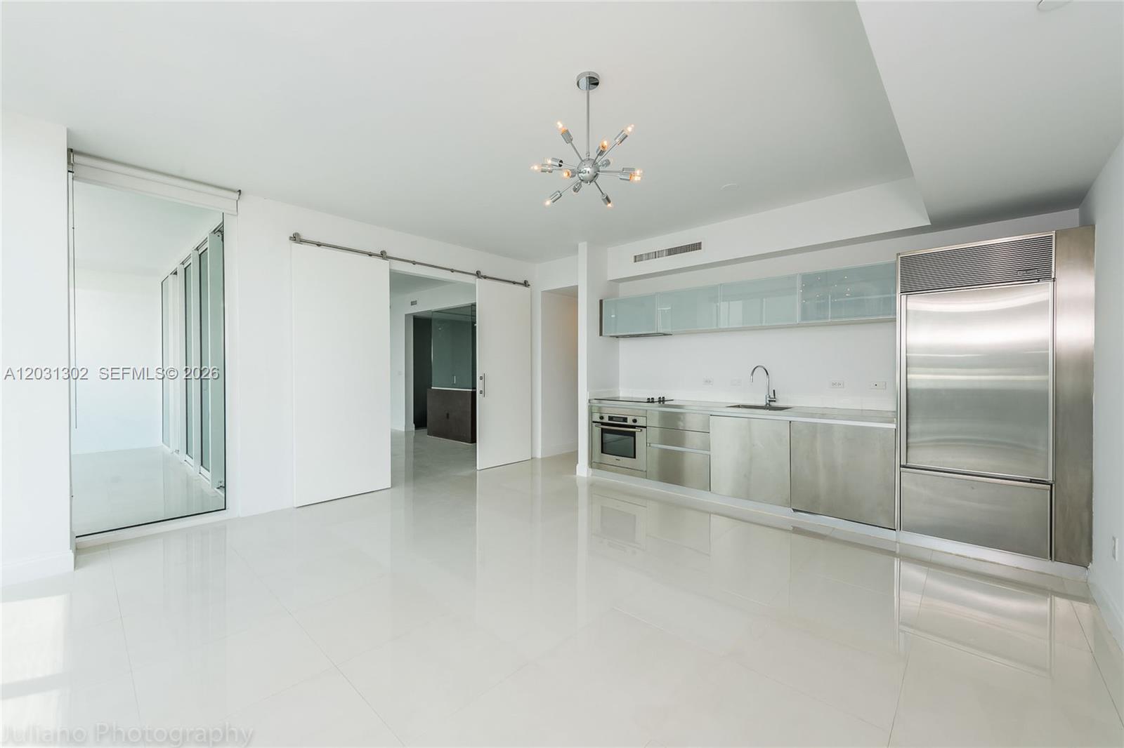 A modern kitchen with stainless steel appliances and white cabinetry opens into a living area — 1040 Biscayne Blvd # 1205, Miami FL 33132, MIAMI, FL