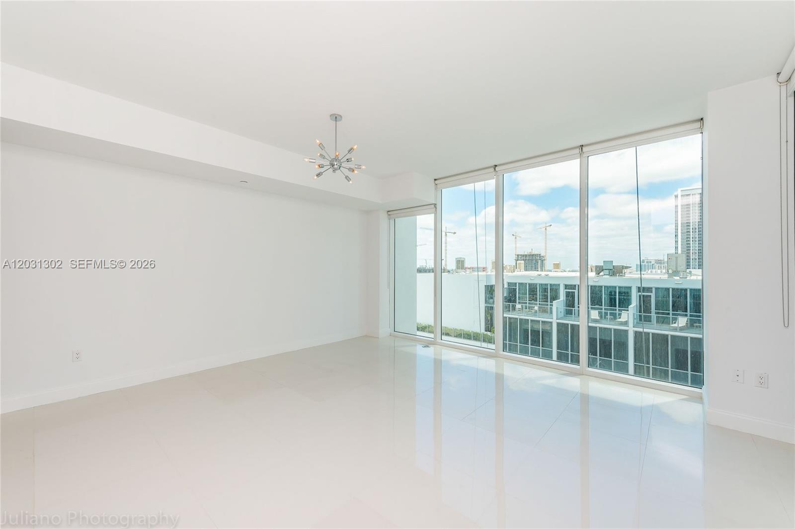 An empty room features white walls, polished tile floors, a modern chandelier, and floor-to-ceiling windows — 1040 Biscayne Blvd # 1205, Miami FL 33132, MIAMI, FL