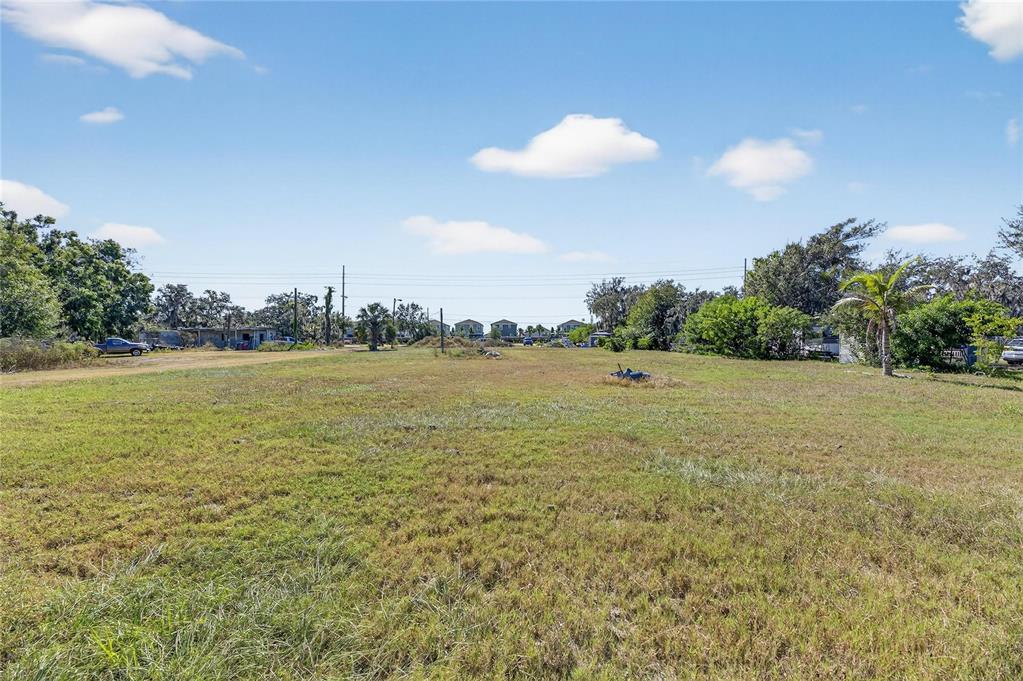 A wide, grassy vacant lot under a blue sky with scattered clouds and distant trees — 11734 RHODINE ROAD, RIVERVIEW, FL