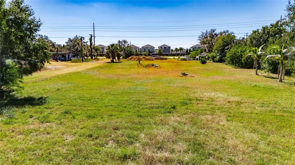 A wide, grassy vacant lot features scattered trees and power lines under a clear sky — 11734 RHODINE ROAD, RIVERVIEW, FL