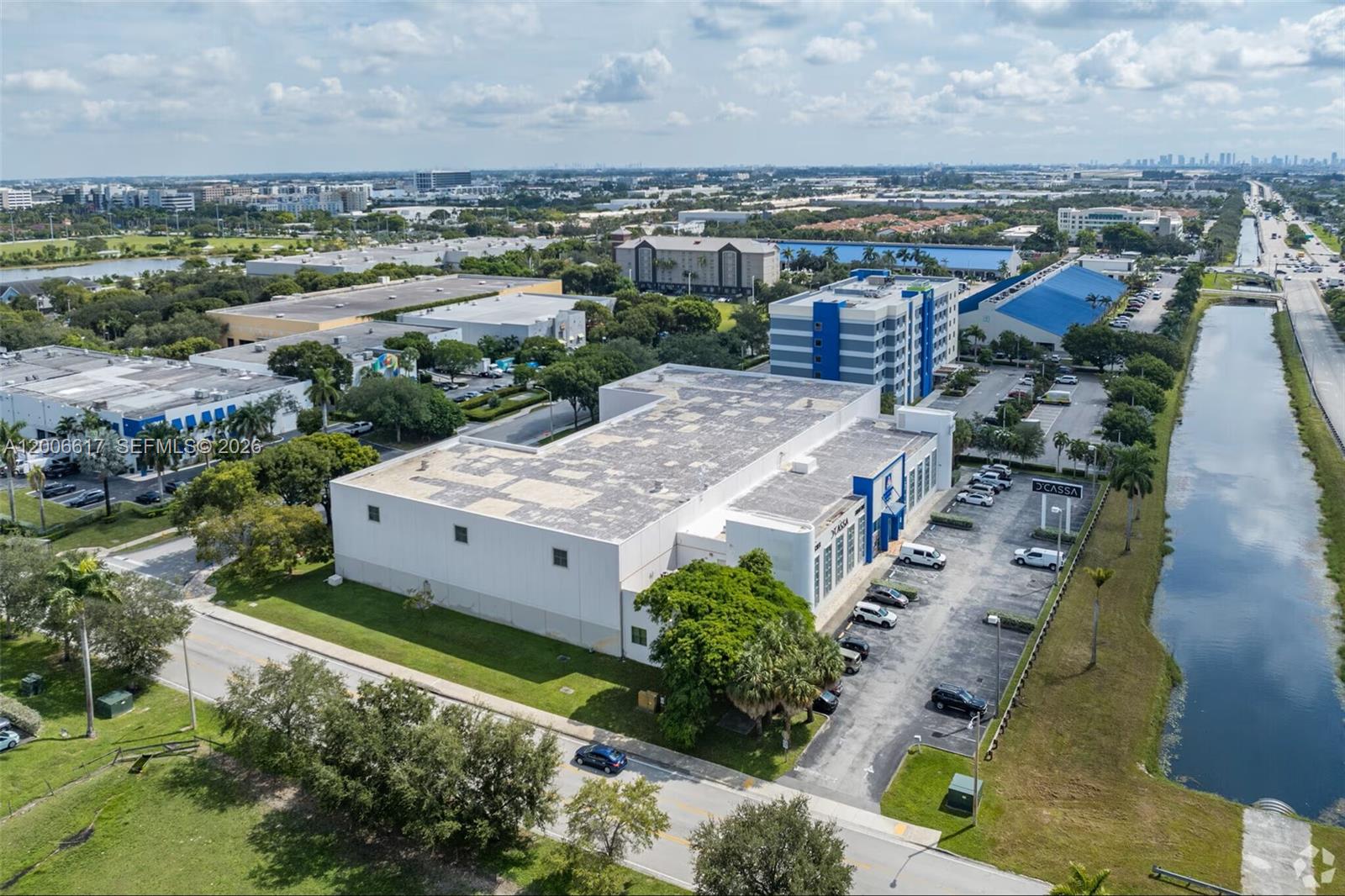 An aerial view shows a commercial building with a parking lot next to a canal — 8975 NW 26th St, Doral FL 33172, DORAL, FL