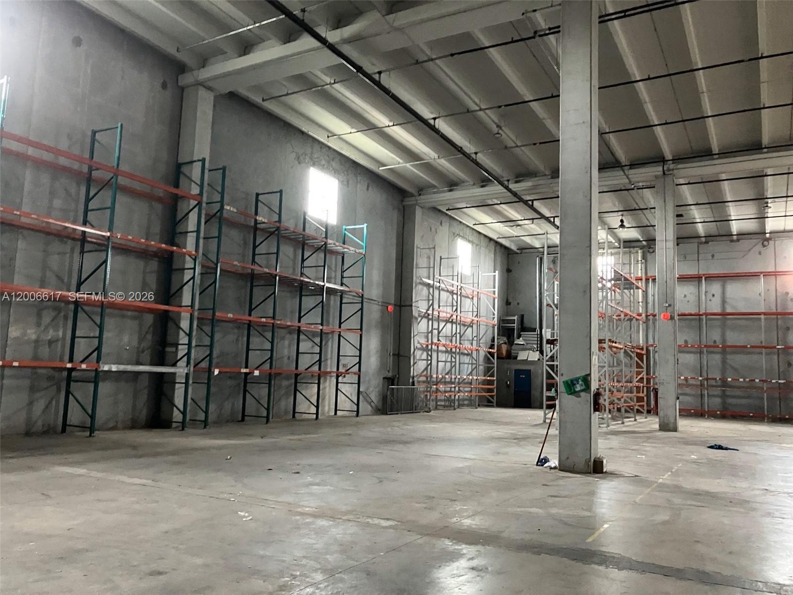 An empty warehouse interior features concrete walls, high ceilings, and rows of metal storage racks — 8975 NW 26th St, Doral FL 33172, DORAL, FL