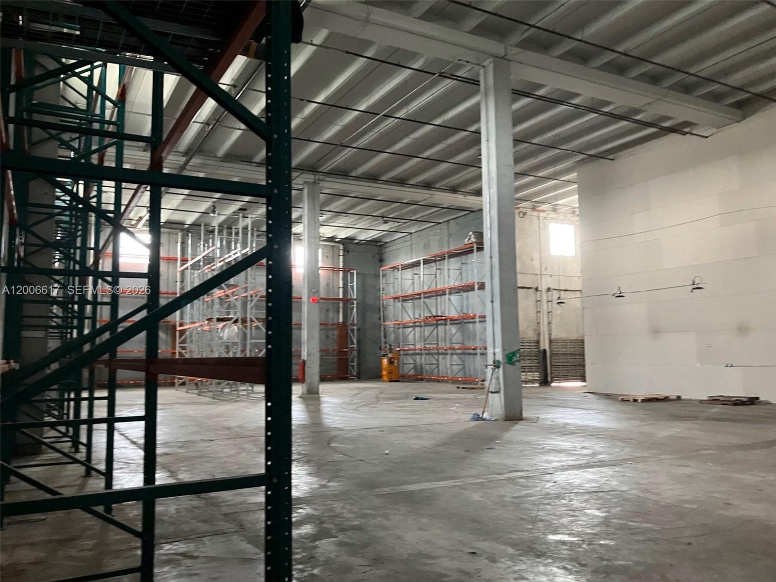 An expansive warehouse interior features high ceilings, concrete floors, and multiple rows of metal shelving — 8975 NW 26th St, Doral FL 33172, DORAL, FL