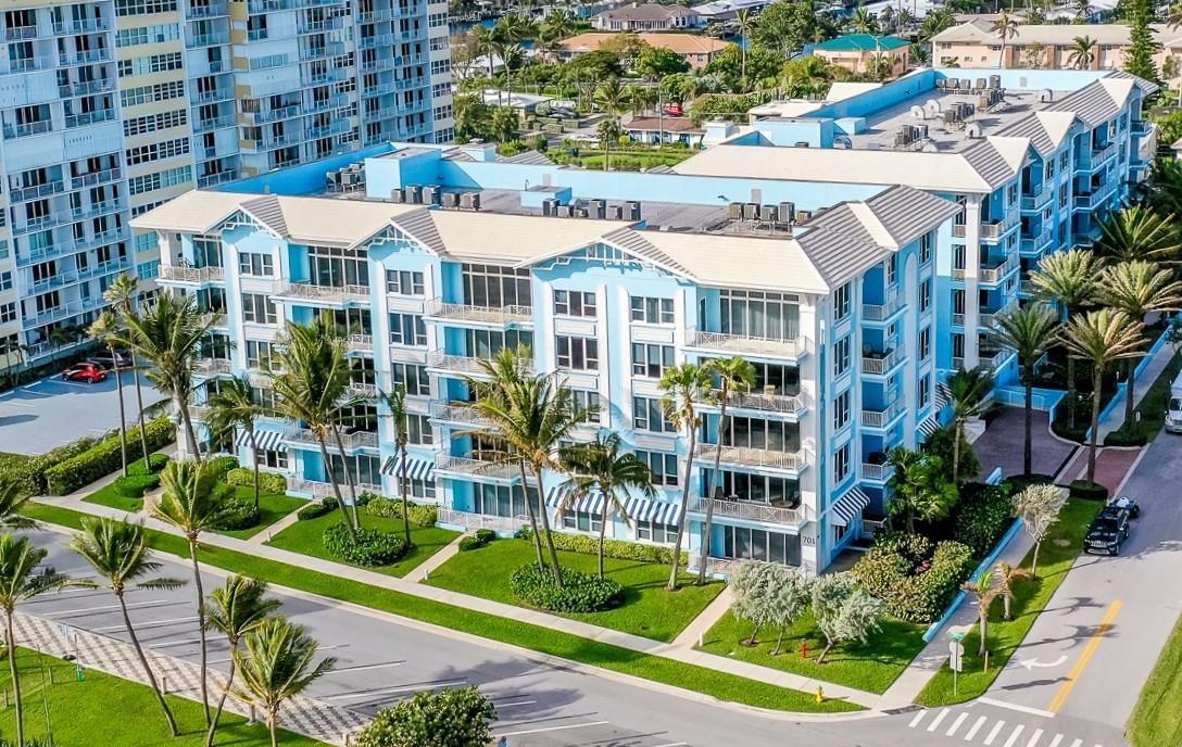 An aerial view of a multi-story light blue residential building surrounded by palm trees — 701 SE 21st Avenue # 304, Deerfield Beach FL 33441, DEERFIELD BEACH, FL