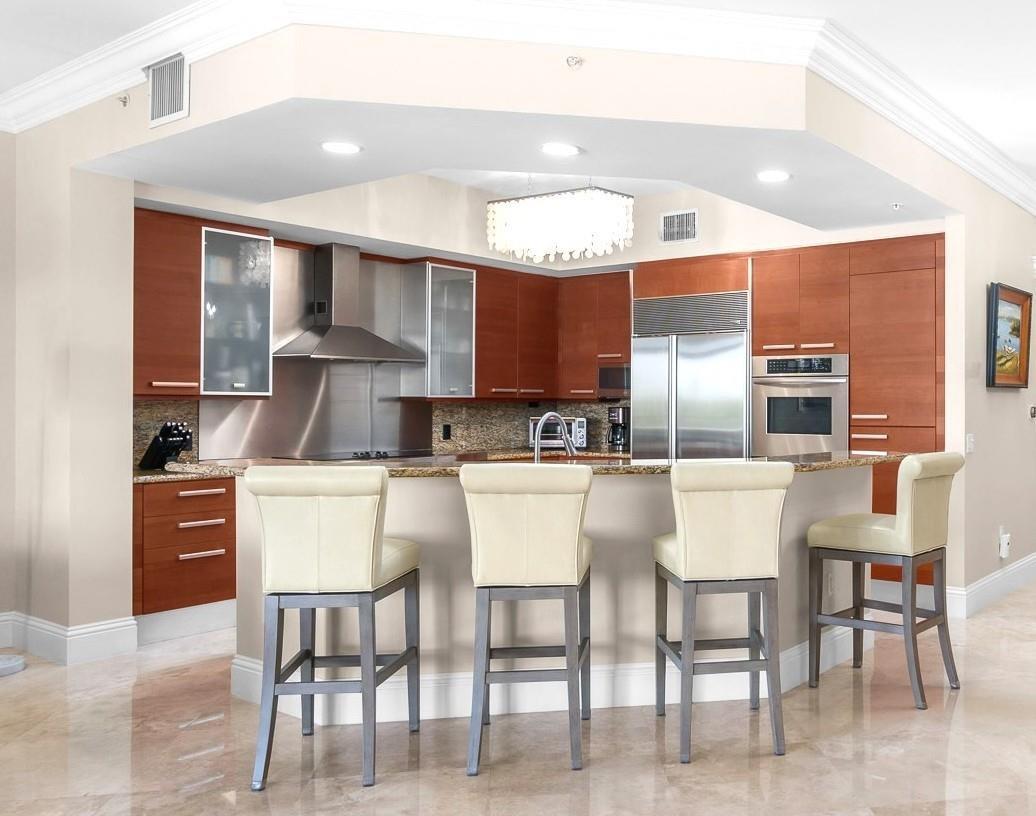 A kitchen with cherry wood cabinets, stainless steel appliances, granite countertops, and four bar stools — 701 SE 21st Avenue # 304, Deerfield Beach FL 33441, DEERFIELD BEACH, FL
