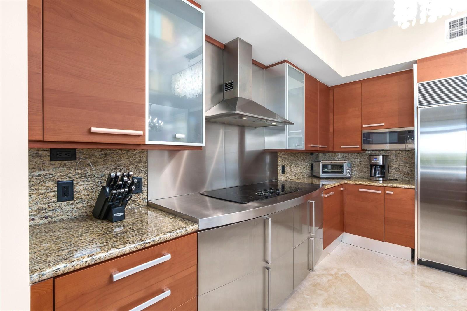 A modern kitchen features wood cabinets, stainless steel appliances, a metal backsplash, and granite countertops — 701 SE 21st Avenue # 304, Deerfield Beach FL 33441, DEERFIELD BEACH, FL