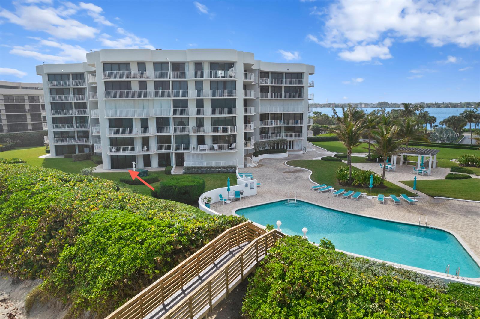 An exterior view of a multi-story white condominium building with a pool and wooden walkway — 3360 S Ocean Boulevard, Palm Beach FL 33480, PALM BEACH, FL