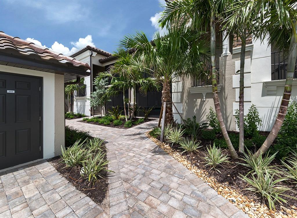 A paved walkway leads toward the entrance of a house with palm trees and landscaping — 5548 PALMER CIRCLE UNIT 103, BRADENTON, FL