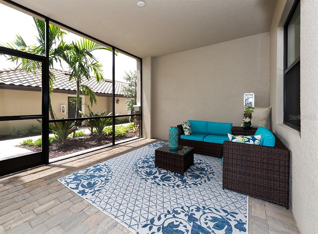 A screened-in patio features a wicker sofa, a patterned rug, and a view of landscaping — 5548 PALMER CIRCLE UNIT 103, BRADENTON, FL