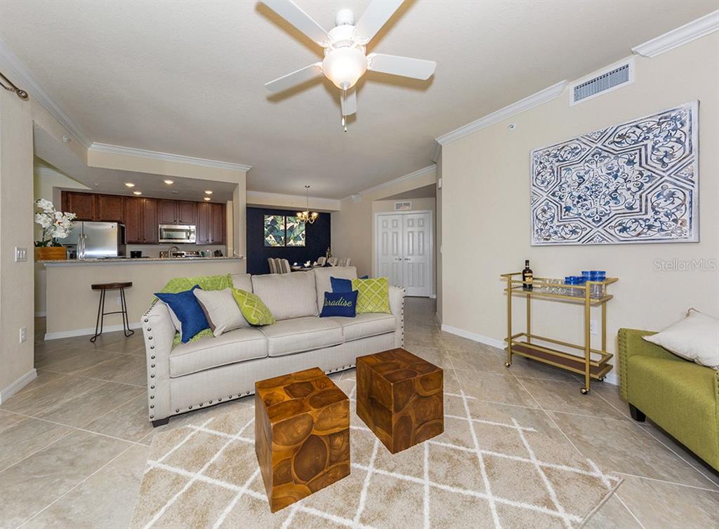 A living room features a beige sofa, two wooden cube ottomans, and a bar cart — 5548 PALMER CIRCLE UNIT 103, BRADENTON, FL