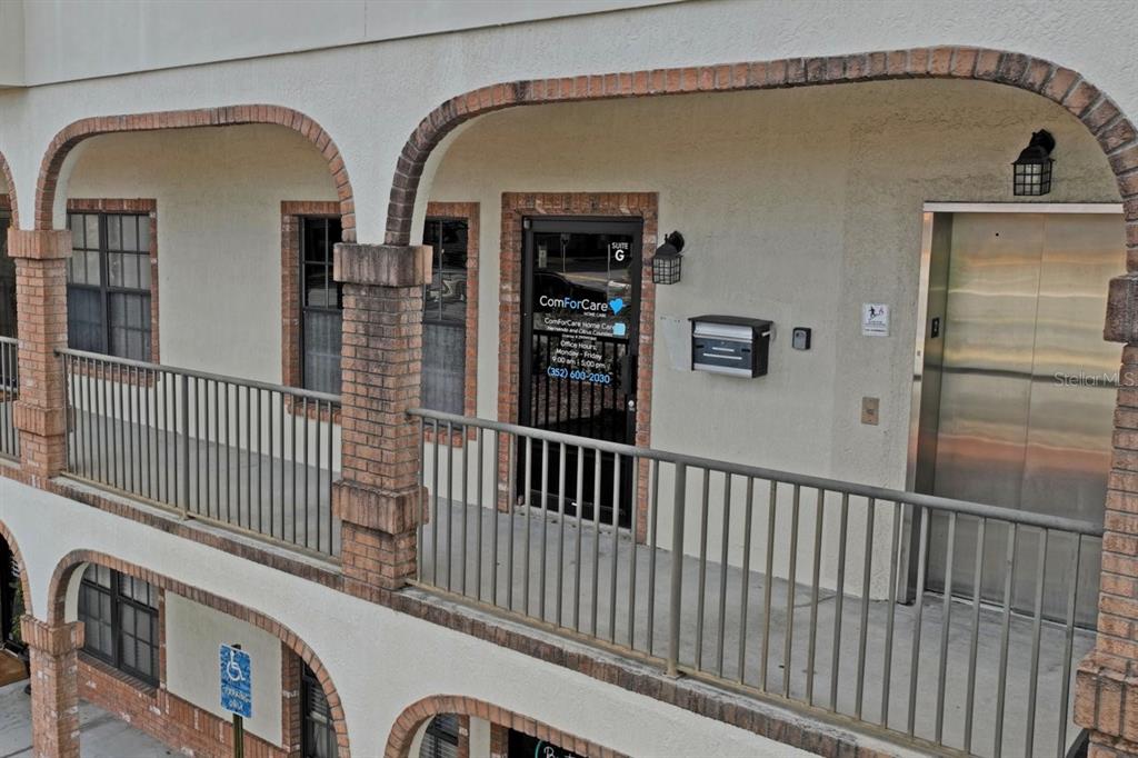 An exterior view of a second-story office balcony with a brick-arched walkway and elevator — 5330 SPRING HILL DRIVE UNIT A, SPRING HILL, FL