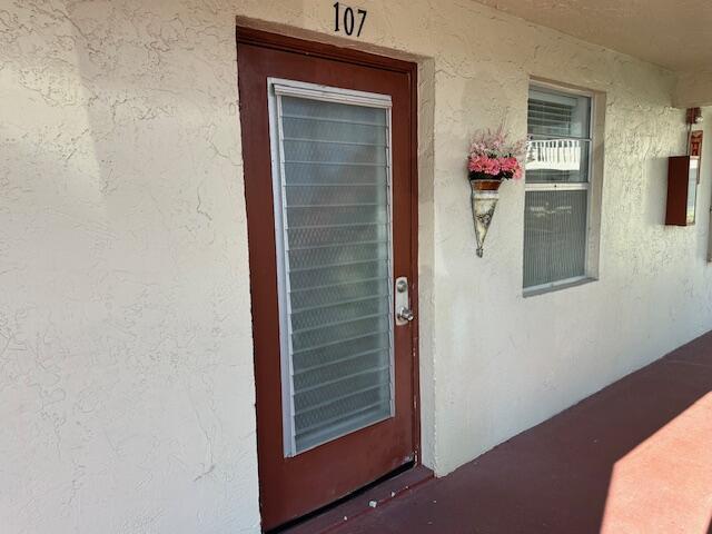 A brown door with a screen insert and a wall-mounted flower basket beside a window — 21 Abbey Lane # 107, Delray Beach FL 33446, DELRAY BEACH, FL