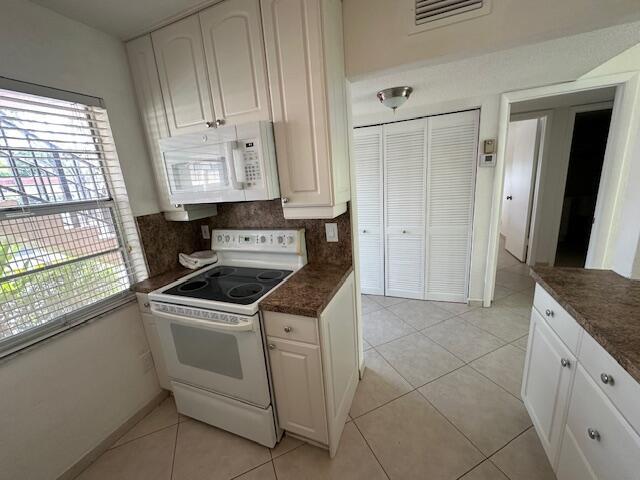 A kitchen features white cabinets, a white electric stove, and tile flooring — 21 Abbey Lane # 107, Delray Beach FL 33446, DELRAY BEACH, FL