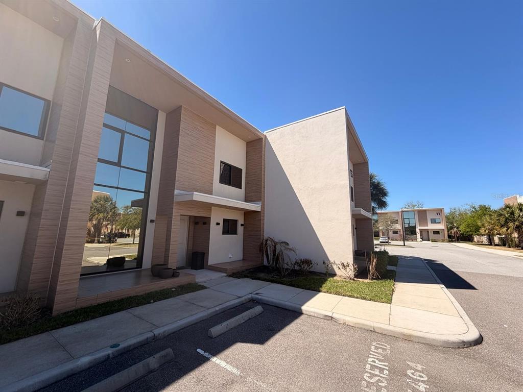 A modern two-story townhouse exterior with a glass facade and a reserved parking space — 7464 BROOKLYN DRIVE, KISSIMMEE, FL