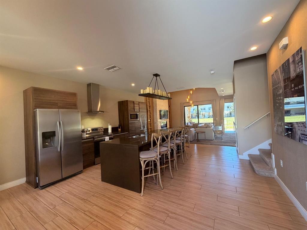 A modern kitchen with wood cabinetry and a large island overlooks a living area — 7464 BROOKLYN DRIVE, KISSIMMEE, FL