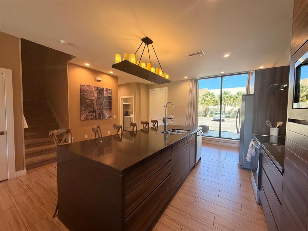 A modern kitchen features a large dark island, wood-look tile floors, and a candle-style chandelier — 7464 BROOKLYN DRIVE, KISSIMMEE, FL