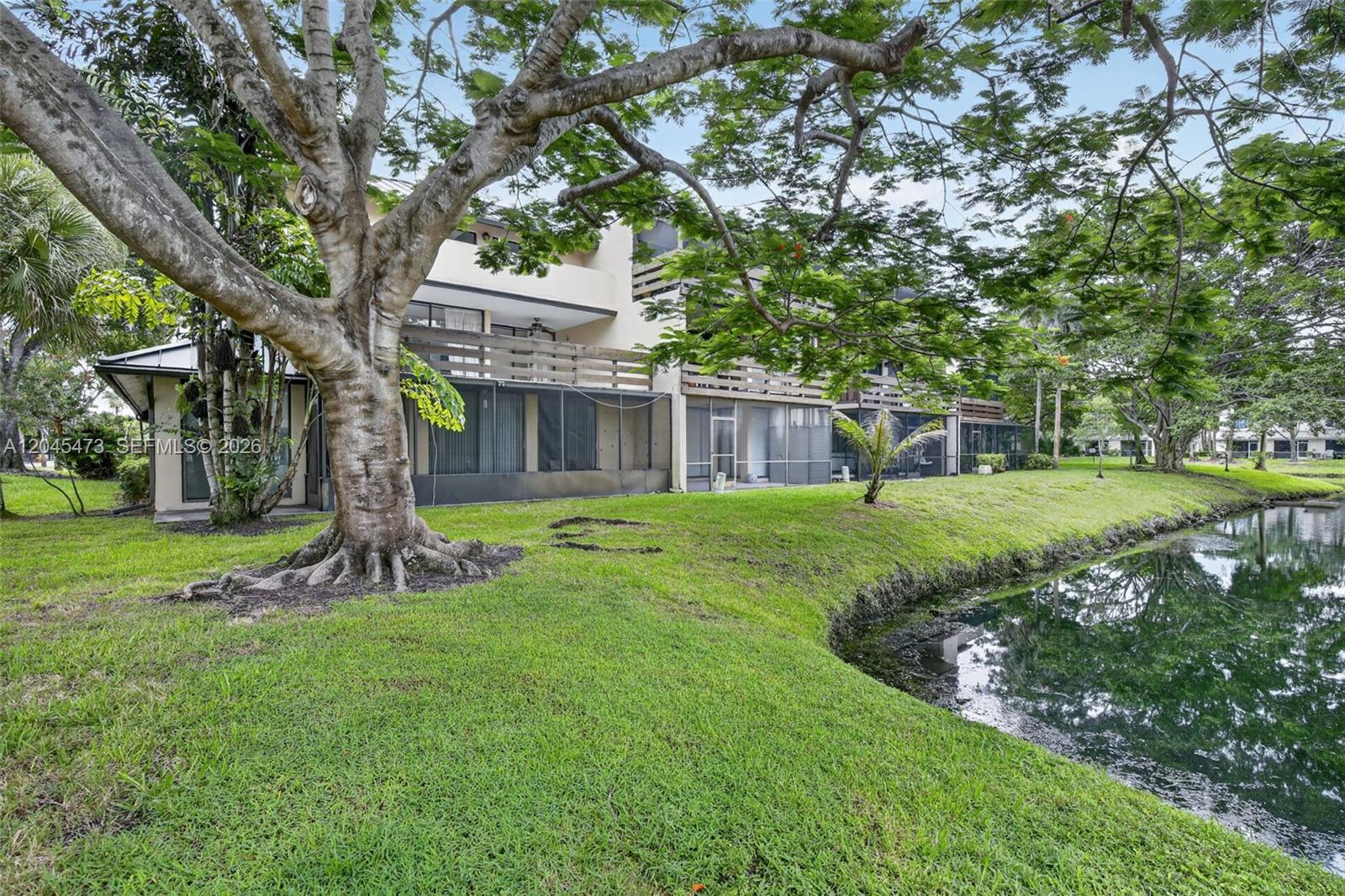 A multi-story apartment building sits beside a canal with a large tree in the foreground — 120 SW 96th Ter # 204, Plantation FL 33324, PLANTATION, FL