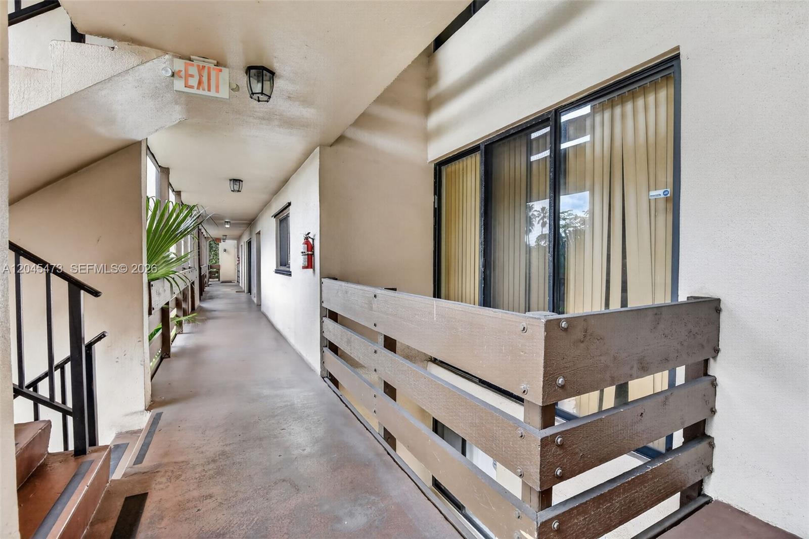 An outdoor apartment building walkway features a wooden railing, a fire extinguisher, and an exit sign — 120 SW 96th Ter # 204, Plantation FL 33324, PLANTATION, FL